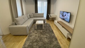 Una sala de estar moderna con un sofá modular, una mesita blanca, un televisor en la pared y una alfombra gris.
