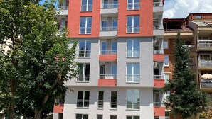 Un edificio residencial de varios pisos con balcones, zona de estacionamiento y árboles.