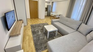 Una sala de estar moderna con un sofá gris, una mesa de centro blanca y un televisor de pantalla plana sobre un soporte de madera.