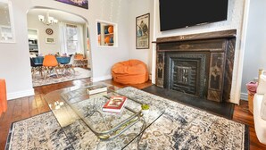 A living room with a fireplace, a television, and a dining area with chairs and a table. - Pet-Friendly Home w/ Fire Pit, Mexican War Streets. Walk to PNC Park! (Pittsburgh)