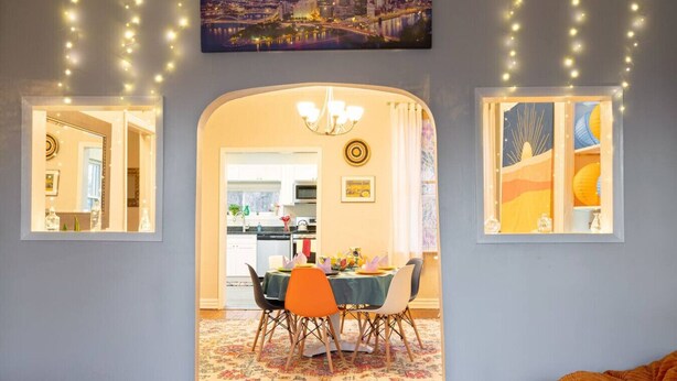 A dining area with a table, chairs, and a chandelier. There is a kitchen visible through an archway. - Pet-Friendly Home w/ Fire Pit, Mexican War Streets. Walk to PNC Park! (Pittsburgh)