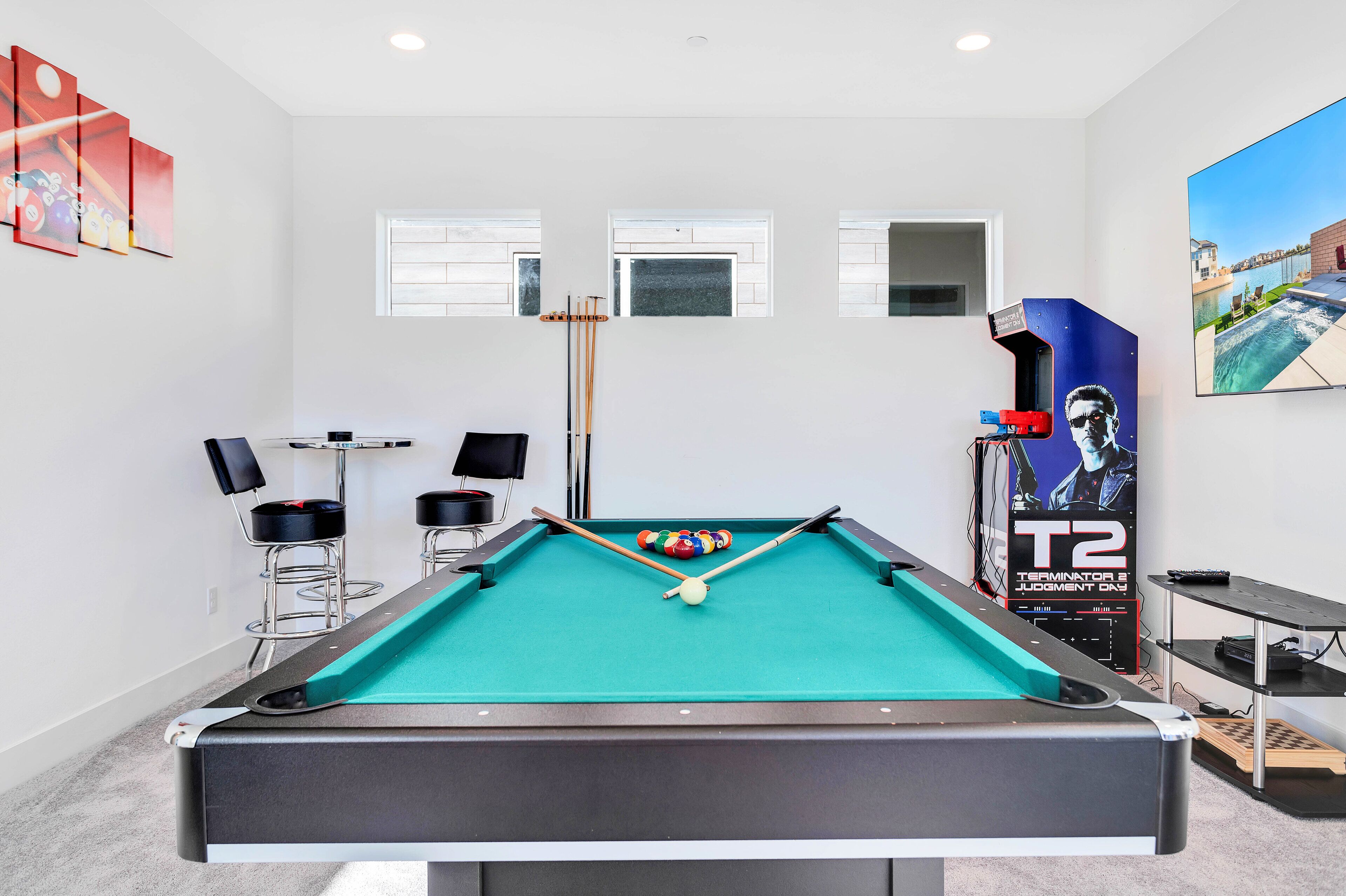 A pool table with a T2 poster, two windows, and a TV screen.