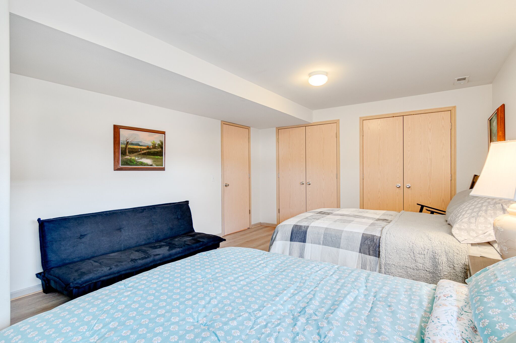 A bedroom with two beds, a bench, and a wardrobe.