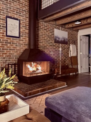 A room with a brick fireplace, a framed map, a painting, and a door.