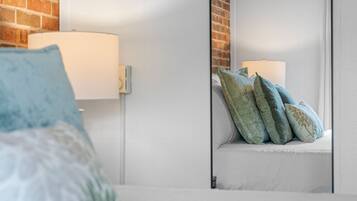 A bedroom with a bed, a nightstand, a mirror, and a brick wall.