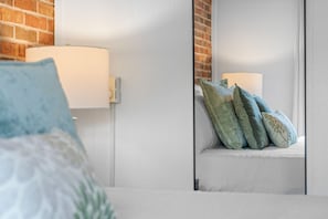 Un dormitorio con una cama, una mesita de noche, un espejo y una pared de ladrillo.