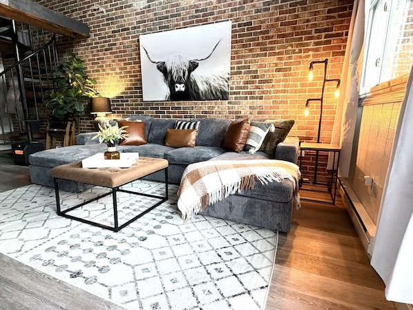 A cozy living room with a sofa, ottoman, coffee table, and a large animal print artwork on the brick wall.