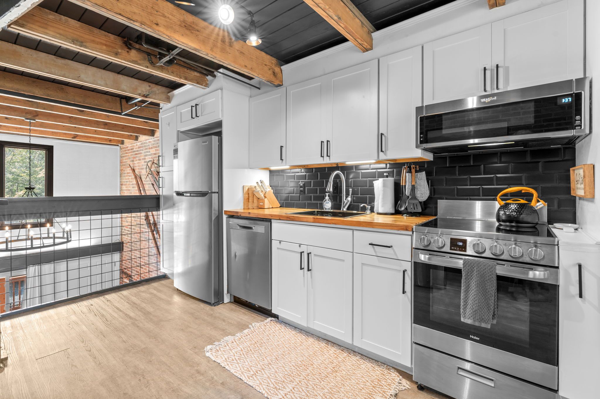 A modern kitchen with stainless steel appliances, a brick wall, and a wooden ceiling.