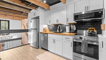 A modern kitchen with stainless steel appliances, a brick wall, and a wooden ceiling.