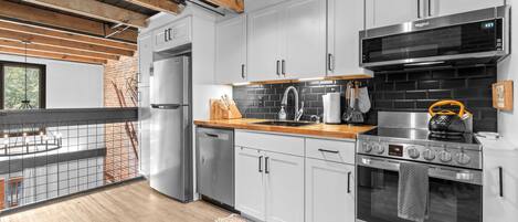 A modern kitchen with stainless steel appliances, a brick wall, and a wooden ceiling.