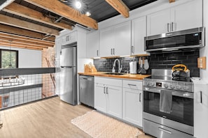 Una cocina moderna con electrodomésticos de acero inoxidable, pared de ladrillo y techo de madera.