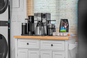 A kitchenette with a coffee maker, a kettle, and a bag of coffee pods on the counter.