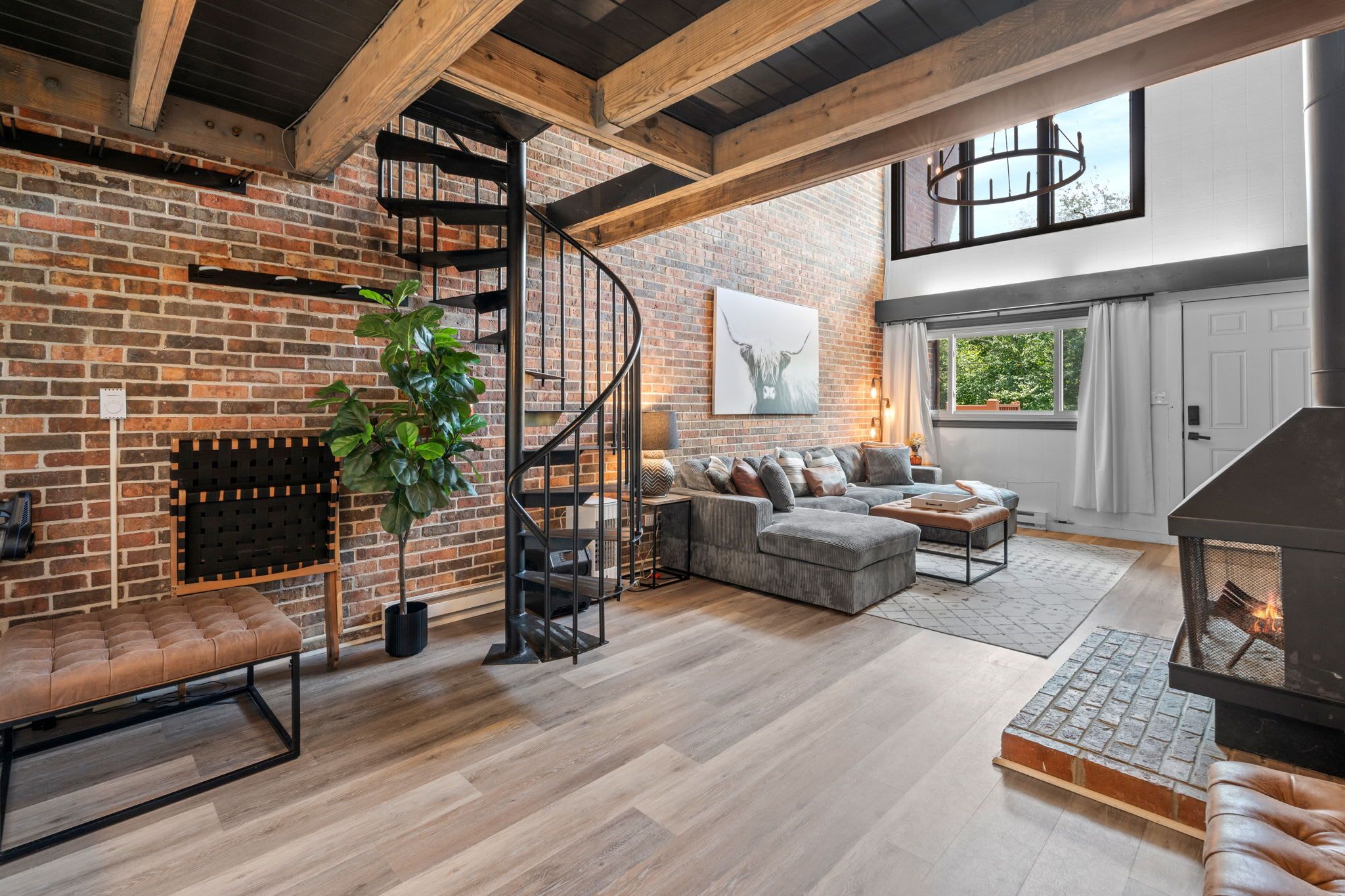 A spacious living area with a brick fireplace, a spiral staircase, a large sofa, and a modern fireplace.