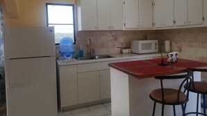 Una cucina con mobili bianchi, un forno a microonde, un lavello e una piccola isola con sgabelli.