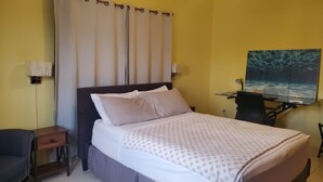 Una camera d'albergo con un letto, una scrivania con un computer, una sedia e una TV a parete.