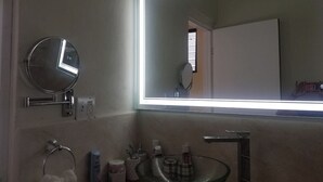Un bagno con uno specchio tondo, un lavandino in vetro e un ampio specchio rettangolare con illuminazione integrata.
