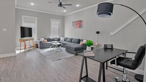 Un soggiorno moderno con un divano componibile, un tavolo da pranzo con una sedia, un televisore e una ventola a soffitto.