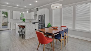 Una cucina moderna con mobili bianchi, un'isola centrale e una zona pranzo con tavolo e sedie in legno.
