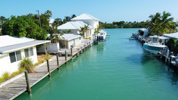 A marina with docked boats, a wooden pier, and a row of white buildings with a sloped roof. - Oceanside waterfront 2/2 home with 55ft dock and paddle equipment (Marathon)