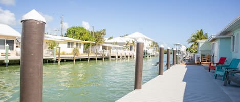 A waterfront dock with moored boats, a wooden walkway, and a row of buildings with white roofs.