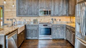 A kitchen with wooden cabinets, stainless steel appliances, and a granite countertop. - Blue Ridge Luxury Cabin with Sunset Views (Mineral Bluff)