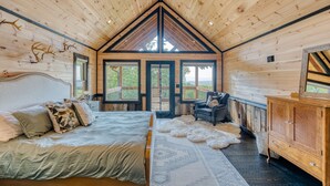A wooden cabin bedroom with a bed, a dresser, and a view of the outdoors. - Blue Ridge Luxury Cabin with Sunset Views (Mineral Bluff)