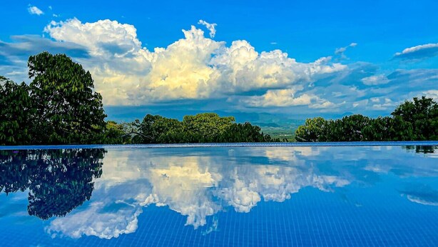 A clear blue sky with clouds, a reflective pool, and dense greenery. - Breathtaking Ocean View Villa, Monkeys Daily, Private Gated Development (Manuel Antonio)