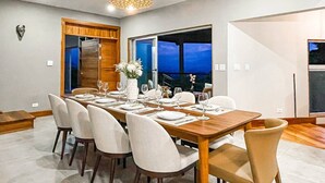 A dining area with a long table set for six, a vase with flowers, and a view of the outside. - Breathtaking Ocean View Villa, Monkeys Daily, Private Gated Development (Manuel Antonio)