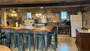 A rustic kitchen with a stone wall, wooden ceiling, and a bar area with stools. - Cozy up in this rustic Stone Lodge and relax by the fireplace (Cleveland)