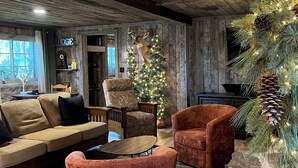 A rustic interior with a wooden ceiling, a sofa, a chair, a Christmas tree, and a stone fireplace. - Cozy up in this rustic Stone Lodge and relax by the fireplace (Cleveland)