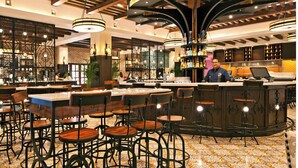 Un restaurante con mesas y sillas redondas, una zona de bar y una barra con un empleado.