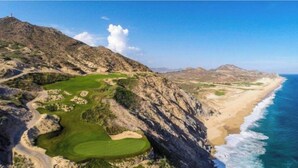 Un paisaje costero con un campo de golf, acantilados rocosos y una playa.