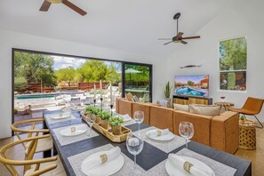 Uma sala de jantar com uma mesa grande posta para seis pessoas, um sofá e uma televisão.