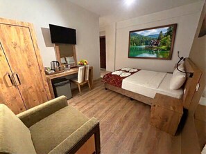 A room with a bed, a desk, a television, a painting, and a wooden wardrobe.