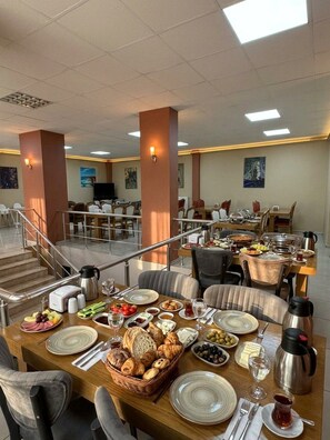 A hotel dining area with multiple tables set for breakfast, featuring a variety of food items and beverages.