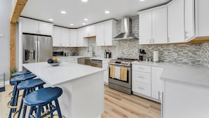 A modern kitchen with white cabinets, a central island with stools, stainless steel appliances, and a patterned backsplash. - Open calender. Washer/dryer. Complementary Netflix. Struck Gold (Reno)