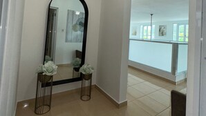 Un pasillo con un espejo grande, dos arreglos florales y vistas a un balcón con ventanas.