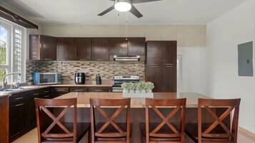 A modern kitchen with dark wooden cabinets, a central island with four wooden chairs, a ceiling fan, and a microwave on the countertop.