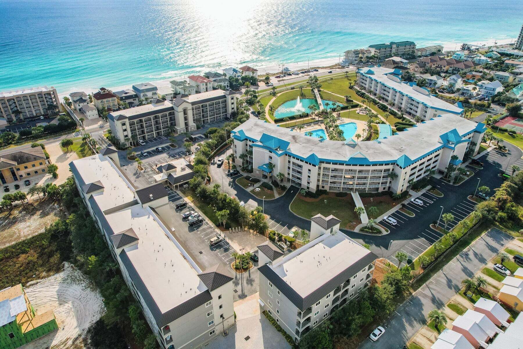 Une vue aérienne d’un hôtel avec une piscine, plusieurs bâtiments et une plage en arrière-plan.