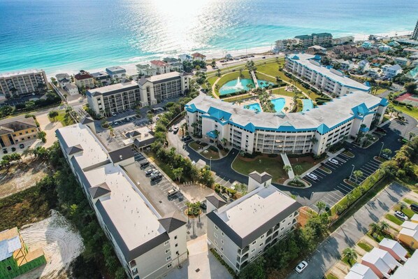 An aerial view of a hotel with a pool, multiple buildings, and a beach in the background.
