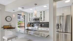 A modern kitchen with a marble countertop, stainless steel appliances, and pendant lighting.
