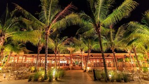 A beachfront hotel with outdoor seating and palm trees.