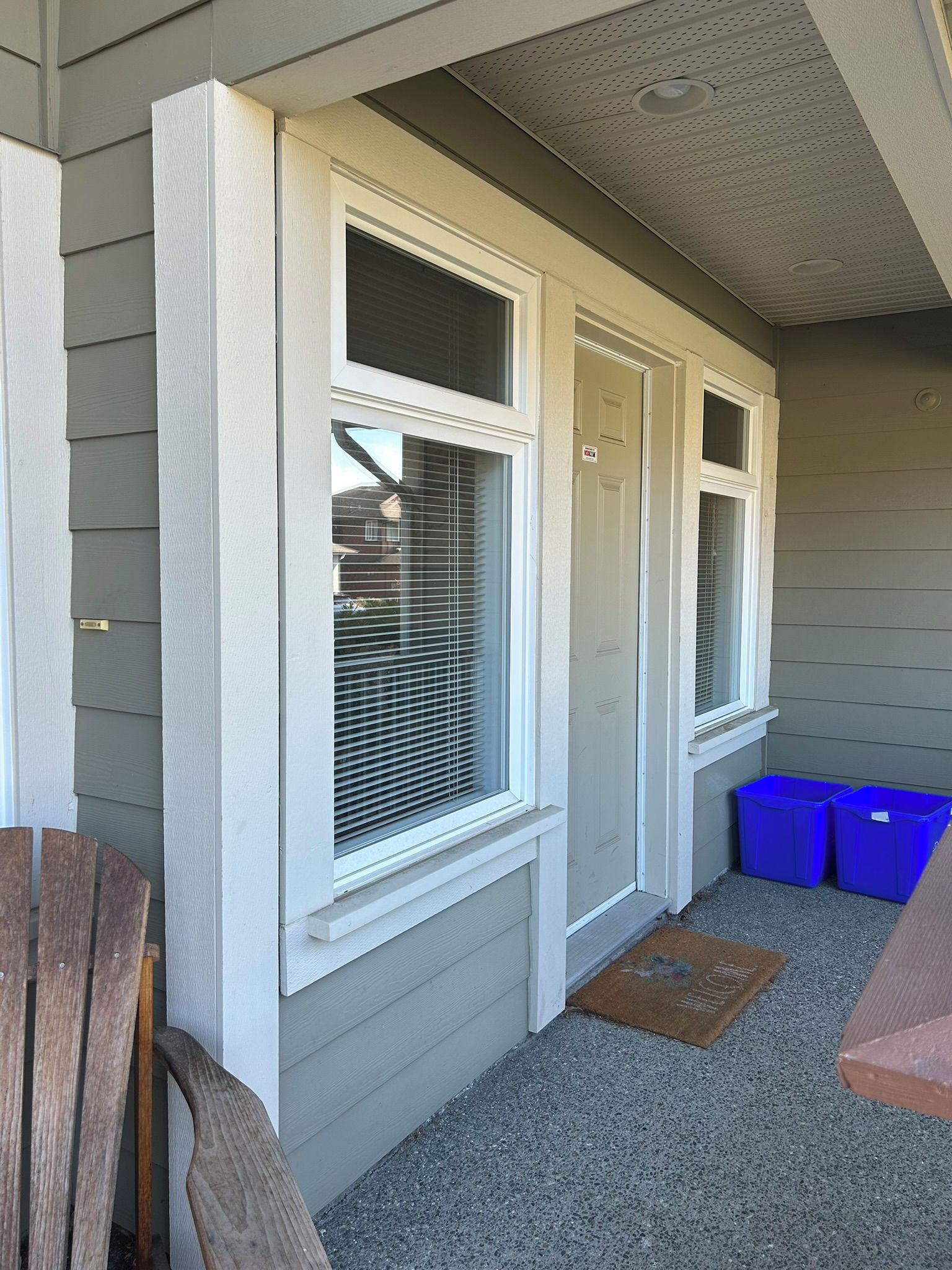 A house exterior with two windows, a door, and a blue trash bin.