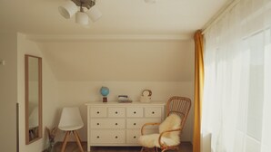 Ein Zimmer mit Holzboden, einem weißen Kommode mit Schubladen, einem Korbsessel, einem Globus und einer Lampe.