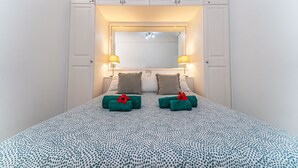 Una habitación de hotel con cama, dos lámparas de noche, un espejo y un armario.