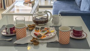 Una mesa de vidrio con té, café y aperitivos, en un salón con un sofá azul.