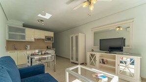 Un espacio habitable compacto con kitchenette, televisor, una mesa de centro de vidrio y un sofá azul.