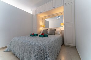 Ein Schlafzimmer mit einem Bett, zwei Kissen, einem Spiegel über dem Bett und einem Nachttisch mit einer Lampe.