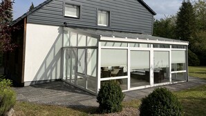 Een modern huis met een grijs dak, een overdekte patio met glazen deuren en een bakstenen schoorsteen.