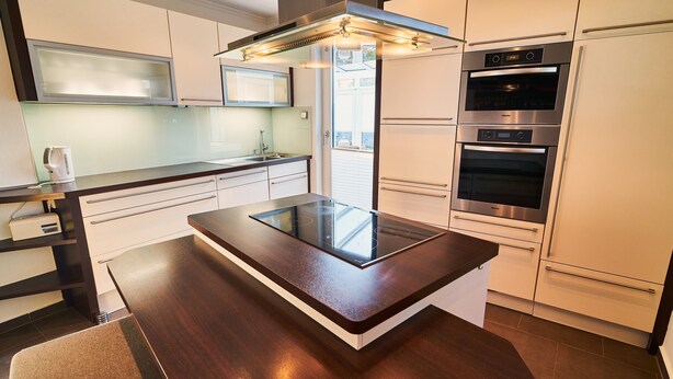Een moderne keuken met een centraal eiland, inbouwovens en een glazen spatwand.